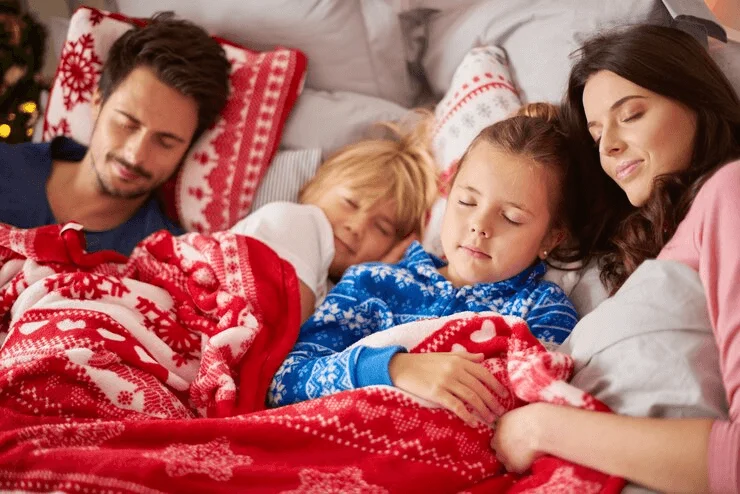 Family members lie close together under a blanket